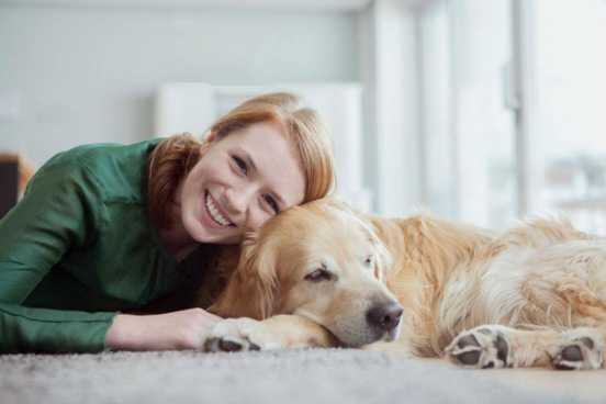 Portrait of smiling young woman lying with her dog on the carpet